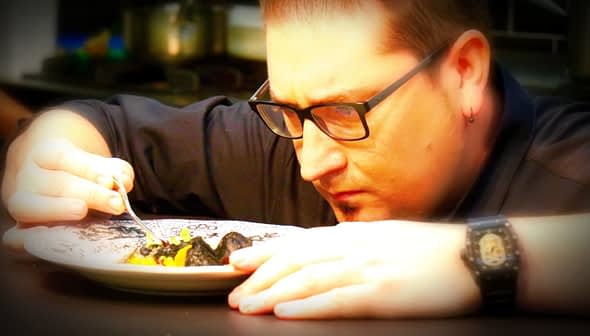 Chef closely inspecting a plate of food with a fork in hand, focused on the dish. - Olive Oil Times