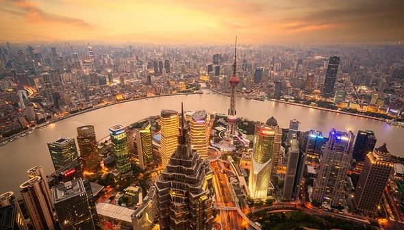 Aerial view of Shanghai's skyline featuring skyscrapers and the Huangpu River during sunset. - Olive Oil Times