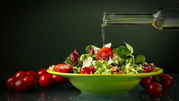 A bowl of mixed salad with cherry tomatoes and olive oil being poured over it. - Olive Oil Times