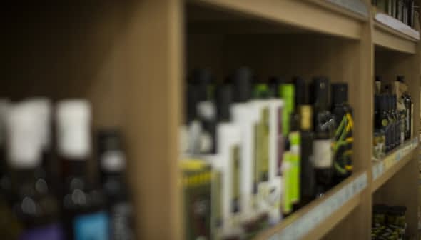 Various bottles of olive oil displayed on wooden shelves in a store. - Olive Oil Times