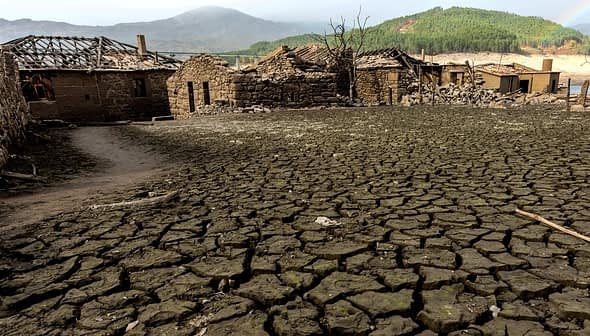 Cracked dry earth with remnants of stone buildings in a desolate landscape. - Olive Oil Times