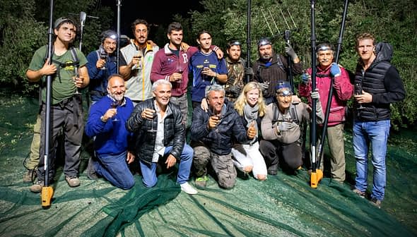 Group of individuals posing together with olive harvesting tools during nighttime. - Olive Oil Times