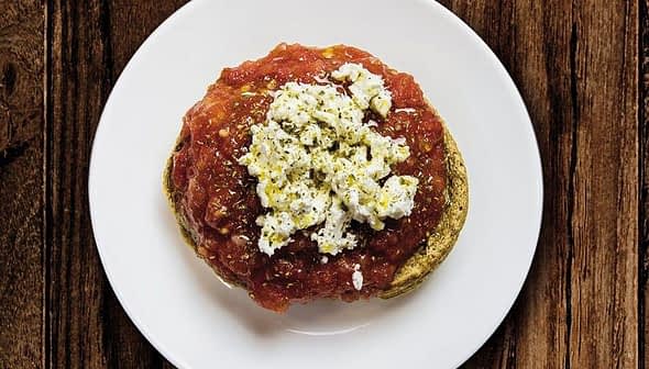 A plate of dakos salad featuring a base of barley rusk topped with tomato sauce and crumbled feta cheese. - Olive Oil Times