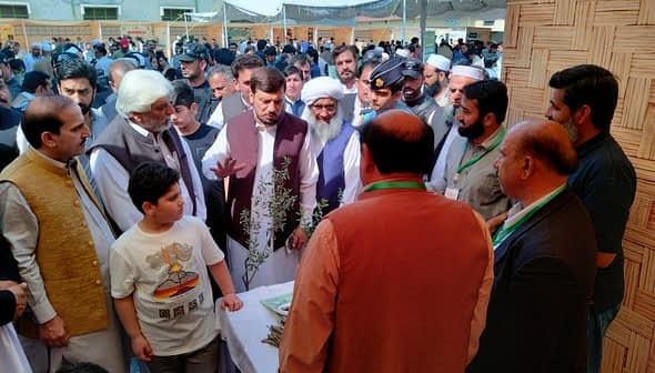 A group of people engaged in discussion at an outdoor event with a table displaying items. - Olive Oil Times