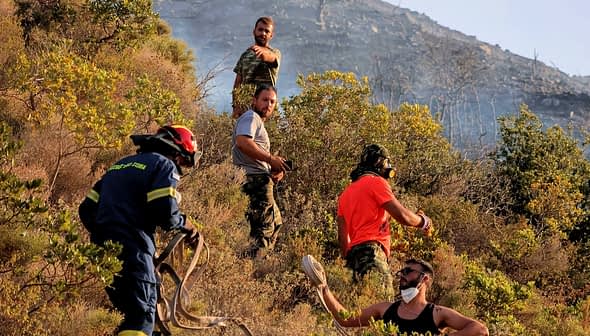 Firefighters and volunteers working together to manage a wildfire in a hilly area with vegetation. - Olive Oil Times