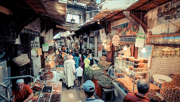 A bustling market scene in a traditional bazaar with various stalls and shoppers. - Olive Oil Times