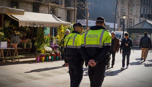 Two police officers in green and black uniforms walking in an urban area with a flower shop in the background. - Olive Oil Times