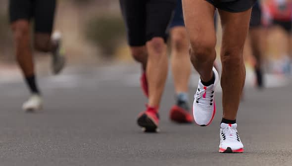 Close-up of a runner's foot in athletic shoes on a road with other runners in the background. - Olive Oil Times