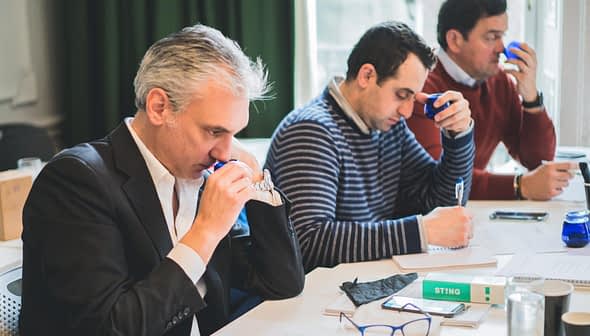 Three men participating in a tasting session, focusing on their individual tasks and using tasting tools. - Olive Oil Times