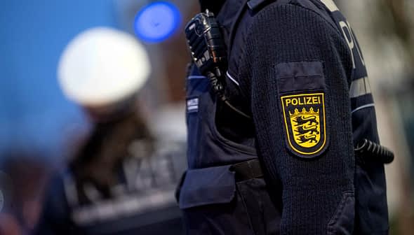 Close-up of a police officer's uniform featuring a badge and radio equipment. - Olive Oil Times