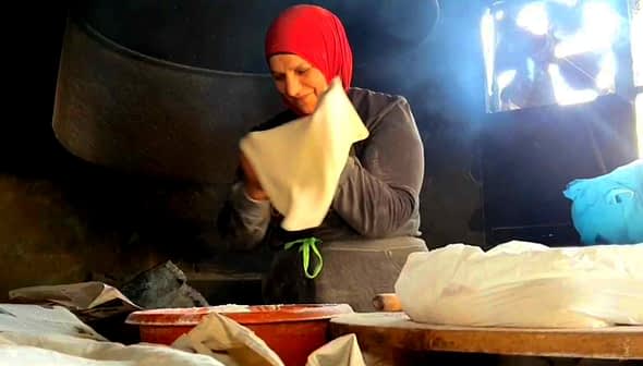 A woman wearing a red headscarf is preparing dough in a kitchen setting. - Olive Oil Times