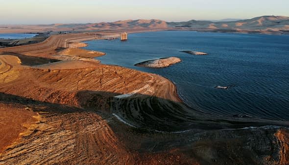 Aerial view of a reservoir with dry land and hills in the background during sunset. - Olive Oil Times