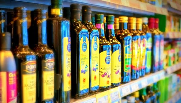 Various bottles of olive oil displayed on a shelf in a grocery store. - Olive Oil Times