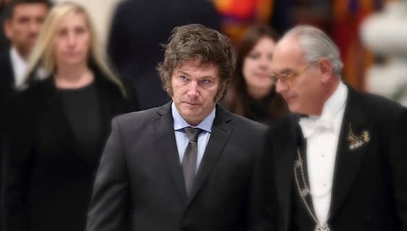 Two men in formal attire walking together at an event, one wearing a suit and tie, the other in a tuxedo. - Olive Oil Times