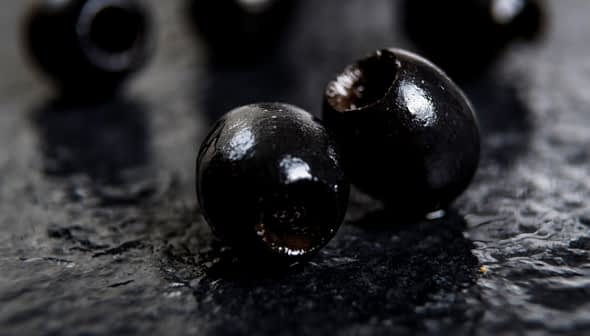 Close-up of black olives placed on a dark textured surface. - Olive Oil Times