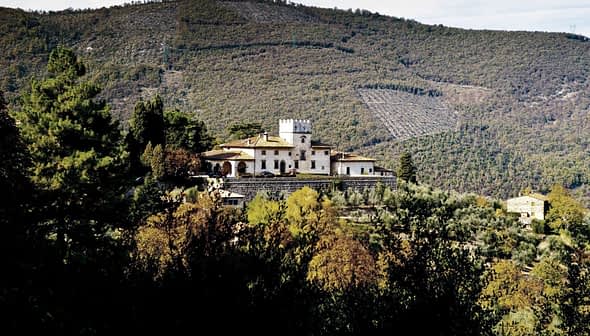 A villa with a tower situated on a hillside in Tuscany, surrounded by trees and rolling hills. - Olive Oil Times