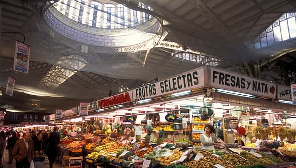Market stall displaying a variety of fruits and vegetables under a large skylight. - Olive Oil Times