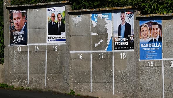 Verschillende politieke campagneposters op een betonnen muur met genummerde secties. Olive Oil Times