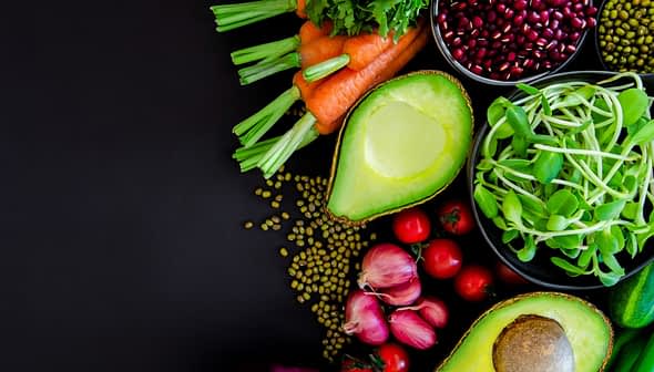 An assortment of fresh vegetables including carrots, celery, and avocado arranged on a dark surface. - Olive Oil Times