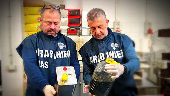 Two men in uniforms holding a metal container and a plastic bottle filled with oil. - Olive Oil Times