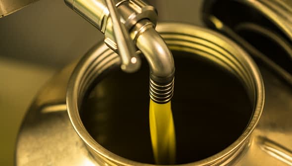 Olive oil being poured from a metal canister into a container. - Olive Oil Times