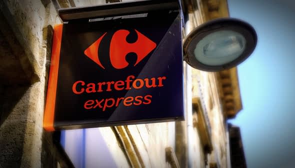 Sign for Carrefour Express featuring a red logo and the name in orange text on a black background. - Olive Oil Times