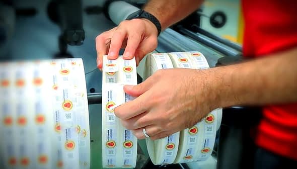 Individual placing labels on a roll of adhesive labels in a manufacturing setting. - Olive Oil Times