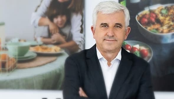 A man with white hair wearing a black suit, standing with arms crossed in front of a blurred background. - Olive Oil Times