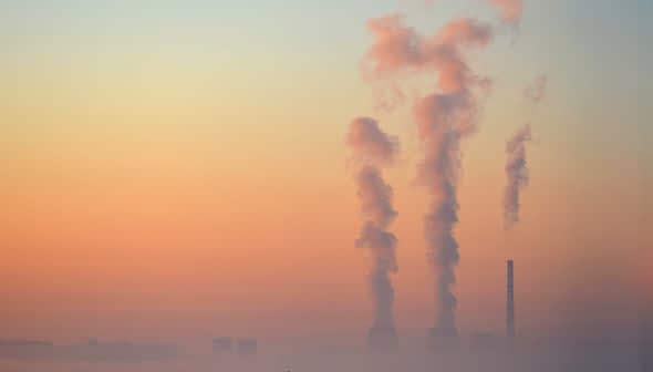 Three smoke stacks emitting vapor into the sky during sunrise with a gradient of colors. - Olive Oil Times