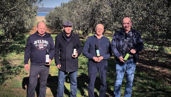 Four men standing in an olive grove, each holding a bottle of olive oil. - Olive Oil Times