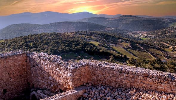Stone ruins overlooking a mountainous landscape during sunset with a colorful sky. - Olive Oil Times