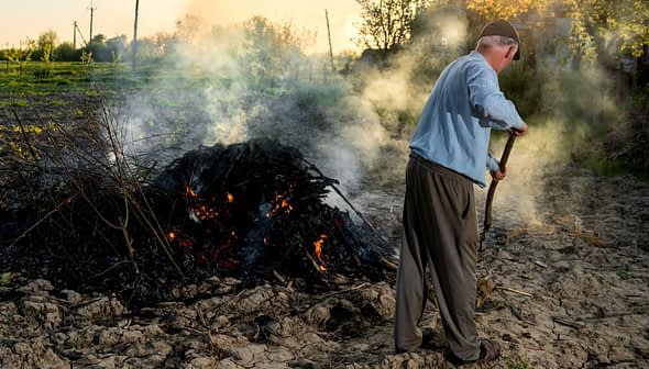 Pojedinac se brine za goruću hrpu grmlja na otvorenom s dimom koji se diže. - Olive Oil Times