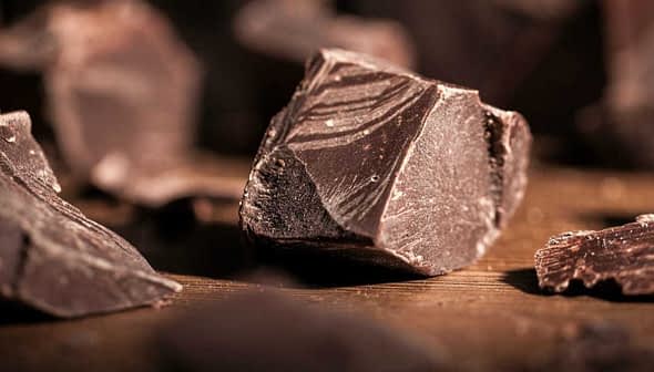 Trozos de chocolate negro esparcidos sobre una superficie de madera con aspecto texturizado. - Olive Oil Times