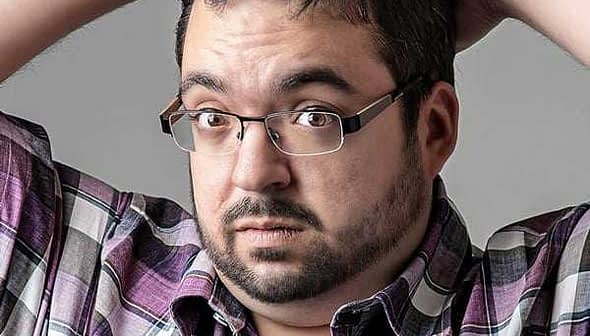 Man with glasses and a plaid shirt holding his head with both hands, looking surprised. - Olive Oil Times