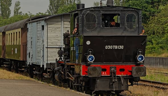 Une locomotive à vapeur noire avec un wagon de passagers bleu et marron dans une gare. - Olive Oil Times