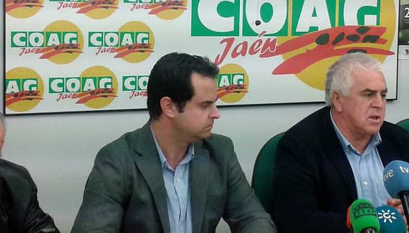 Trije moški sedijo za mizo med tiskovno konferenco z blagovno znamko COAG v ozadju. - Olive Oil Times