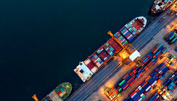 Luftaufnahme von Containerschiffen, die in einem Hafen anlegen, mit bunten Frachtcontainern, die auf dem Deck gestapelt sind. – Olive Oil Times