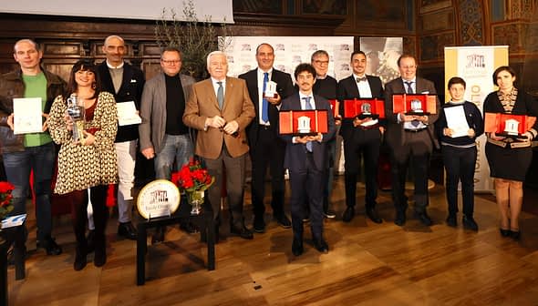 Un gruppo di persone posa con i premi durante una cerimonia, con vari trofei e certificati. - Olive Oil Times