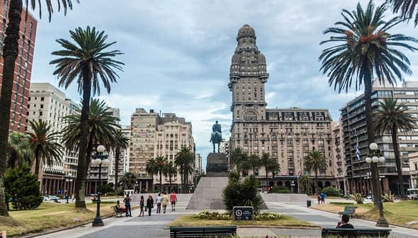 Statue eines Reiters auf der Plaza Independencia, umgeben von Palmen und Gebäuden in Montevideo. - Olive Oil Times