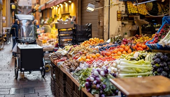 カートや木箱のある市場風の店内に、さまざまな果物や野菜が鮮やかに展示されています。 - Olive Oil Times