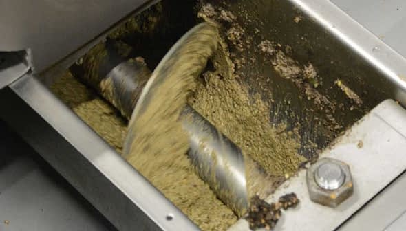 Inside view of an oil extraction machine showing mixing blades and oil paste. - Olive Oil Times