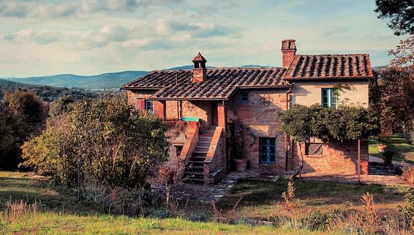 Ferme à deux étages avec un toit en tuiles et des volets bleus entourés de verdure. - Olive Oil Times