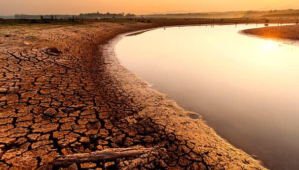Terra secca e screpolata lungo il bordo di un fiume che riflette la luce del tramonto. - Olive Oil Times