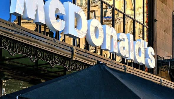 Вывеска ресторана McDonald's с отражающим стеклянным фасадом на заднем плане. - Olive Oil Times