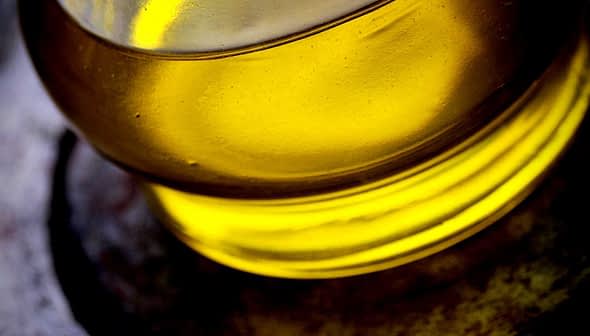 Vista de cerca del aceite de oliva en un recipiente de vidrio con un tono amarillo. - Olive Oil Times