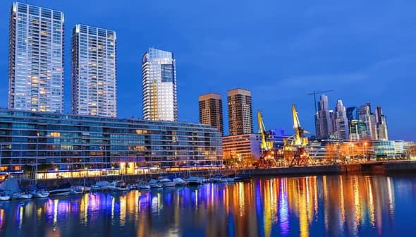 Nachtansicht der Stadtlandschaft von Buenos Aires mit Wolkenkratzern und Spiegelungen am Wasser. - Olive Oil Times
