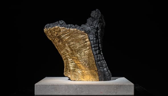 Sculpture présentant une surface noire texturée avec une section dorée, présentée sur une base légère. - Olive Oil Times