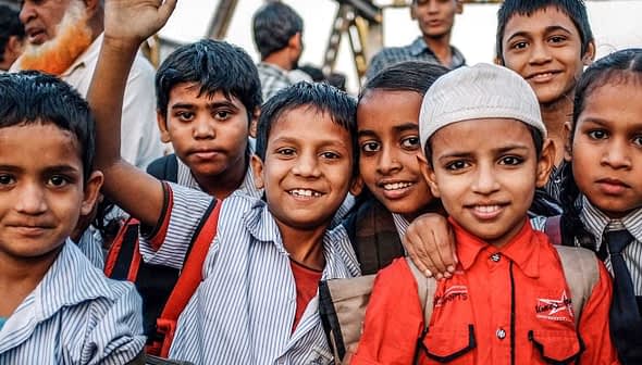 Un gruppo di sette bambini che sorridono alla telecamera, indossando uniformi scolastiche e zaini. - Olive Oil Times