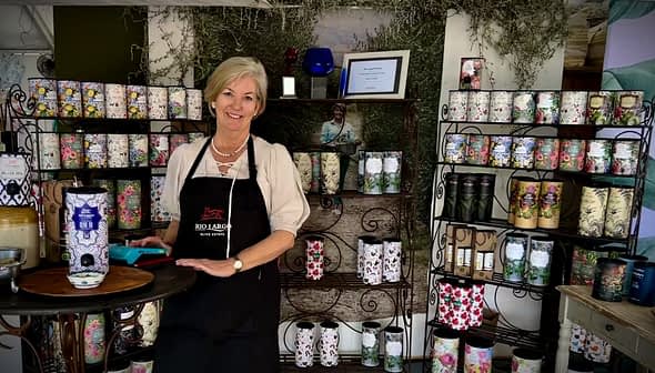 Una donna che indossa un grembiule è in piedi accanto a una mostra di prodotti decorativi sugli scaffali. - Olive Oil Times