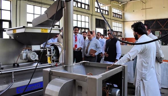 Group of individuals observing an oil extraction machine during a demonstration in a factory setting. - Olive Oil Times